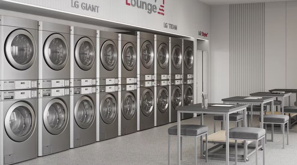 Sala de lavandería de LG con múltiples filas de lavadoras y secadoras comerciales apiladas con acabado en color plata, mesas y sillas dispuestas para los clientes