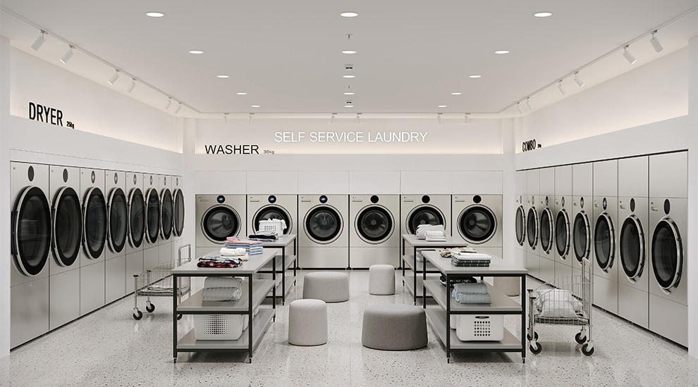 Cuarto de lavado moderno en instalaciones propias con lavadoras y secadoras comerciales LG, mesa central para doblar ropa y amplias ventanas con vista al jardín
