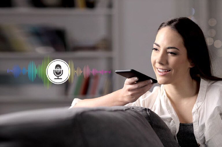 A woman is controlling TV by speaking to a remote control which has voice recognition.