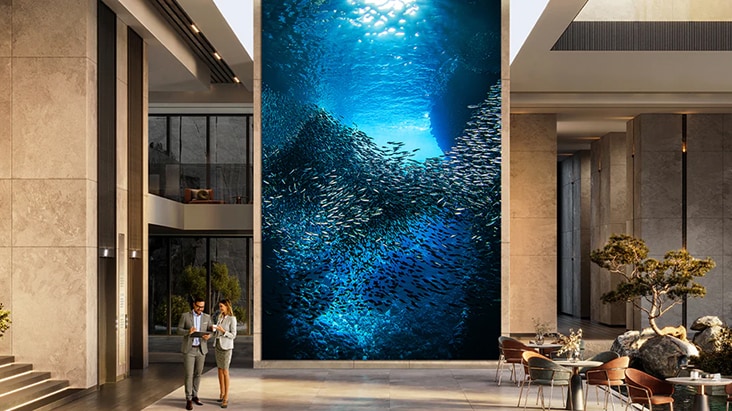 Una señalización LED de LG de gran formato en el vestíbulo de un edificio muestra una vívida escena submarina con un banco de peces. Las soluciones de pantalla digital de LG ofrecen imágenes envolventes para espacios corporativos y comerciales