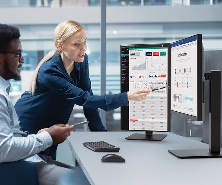 Zwei Mitarbeiter unterschiedlichen Geschlechts unterhalten sich, während sie auf einen Monitor im Büro schauen.