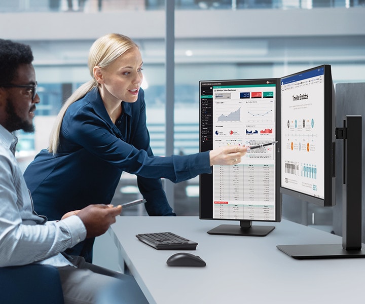 Zwei Mitarbeiter unterschiedlichen Geschlechts unterhalten sich, während sie auf einen Monitor im Büro schauen.	