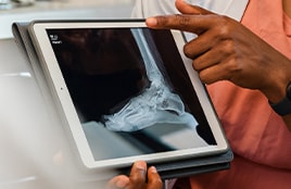 Un professionnel de santé montre une radiographie du pied et de la cheville sur une tablette.