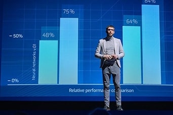 Enceinte professionnelle présentant sur scène devant un grand écran numérique avec des graphiques à barres comparant les pourcentages de performance du réseau neuronal