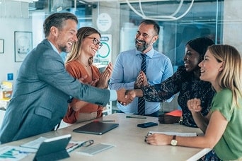 Réunion d’équipe commerciale avec divers professionnels souriants, serrant la main et célébrant le succès dans un environnement de bureau moderne