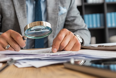Mains examinant les documents avec une loupe représentant la gestion de l’éthique et de la conformité