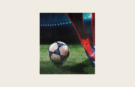 Gros plan d’un joueur de football en cales rouges à côté d’un ballon de football sur un gazon artificiel sous des lumières de stade vives – concept sportif et football.