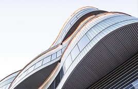 Modern living room interior with a sectional sofa, round coffee tables, and a flat-screen TV displaying abstract graphics. A staircase and floor lamp are in the background.