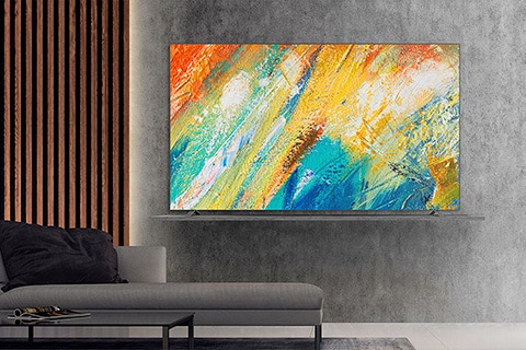 Modern living room with a wall-mounted flat-screen TV displaying a colorful abstract painting, positioned above a gray sofa.