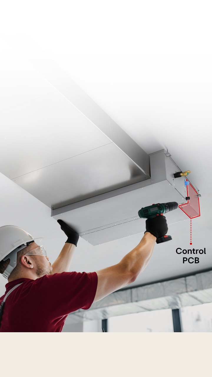 A technician servicing a Ceiling Concealed Ducted Unit, accessing the control PCB through a bottom panel using a power drill.
