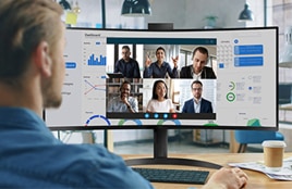 Man participating in a video conference call on an ultrawide curved monitor displaying multiple people and data charts.