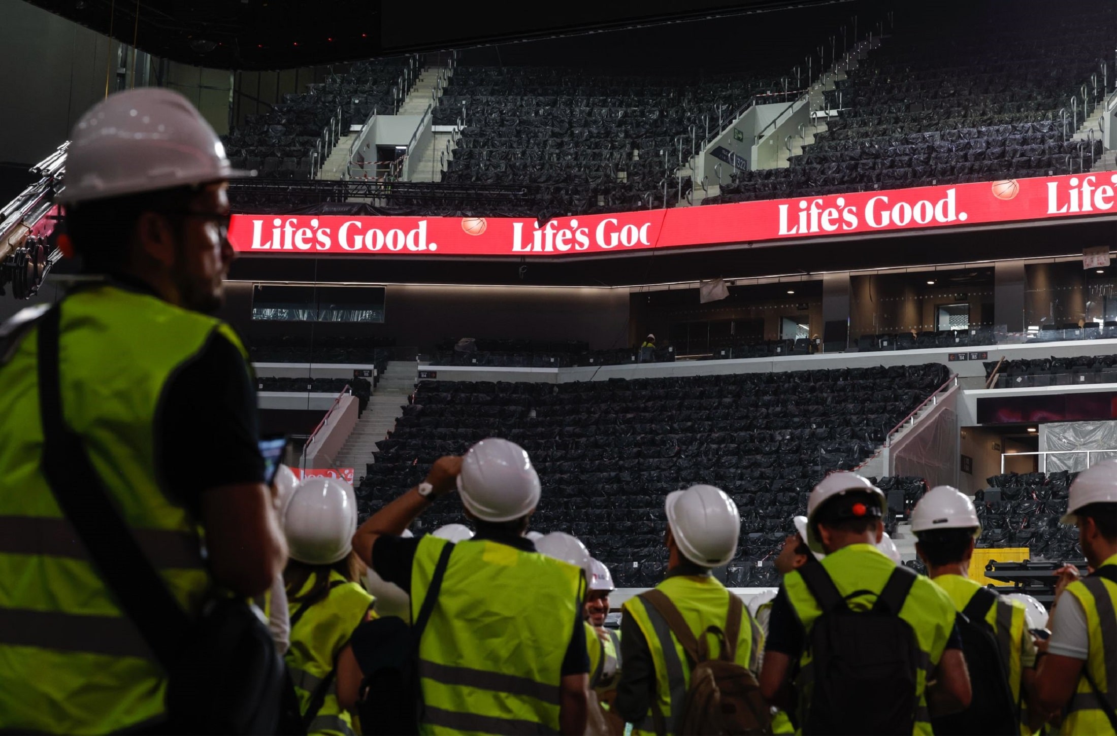 Workers in safety gear observing LED ribbon displays inside Roig Arena, illuminated with LG’s 'Life’s Good' branding around the seating area