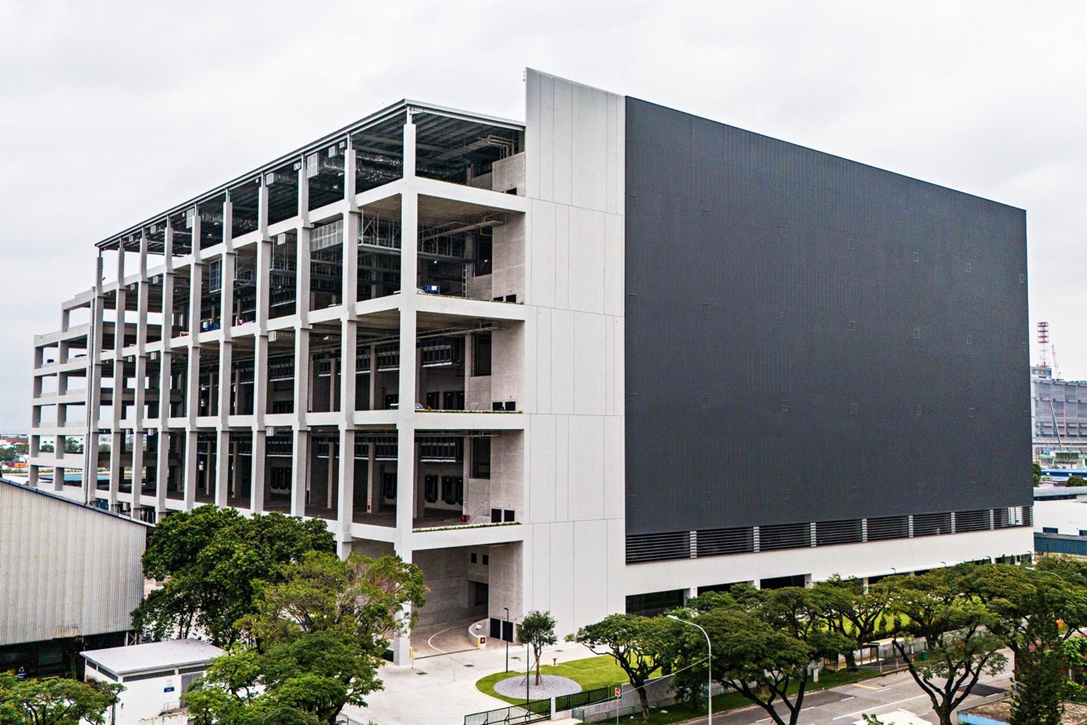 Modern multi-story building with open framework structure and large solid facade, surrounded by trees