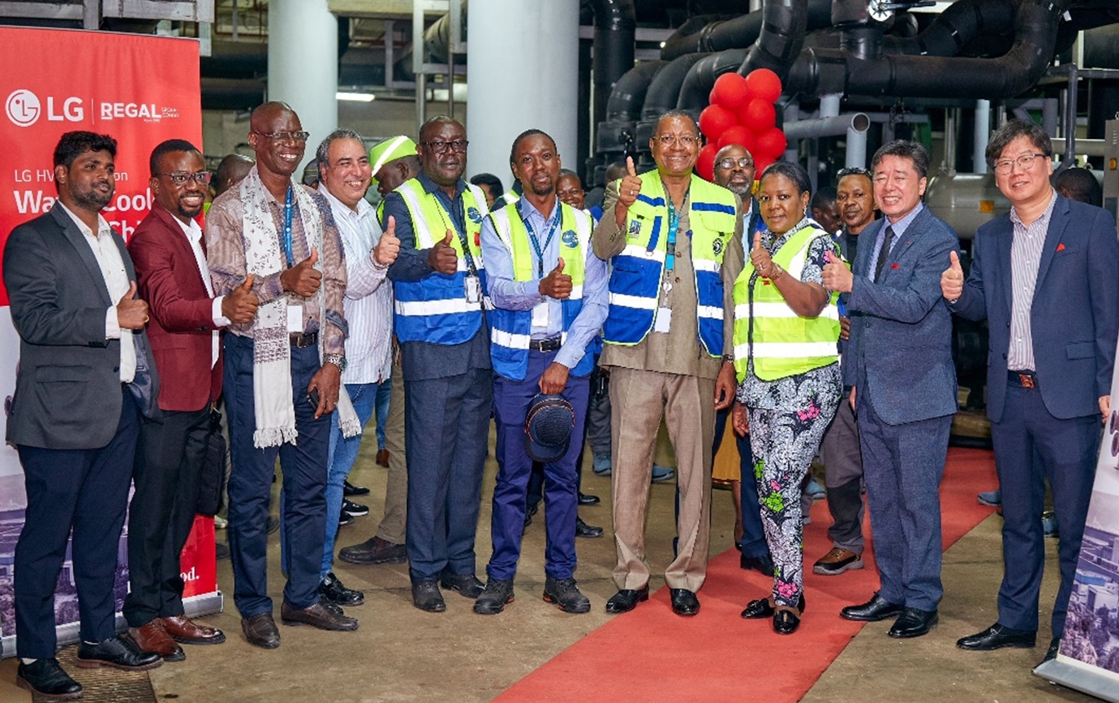 Group of people, including LG representatives and local partners, standing on a red carpet and giving thumbs-up during an official event