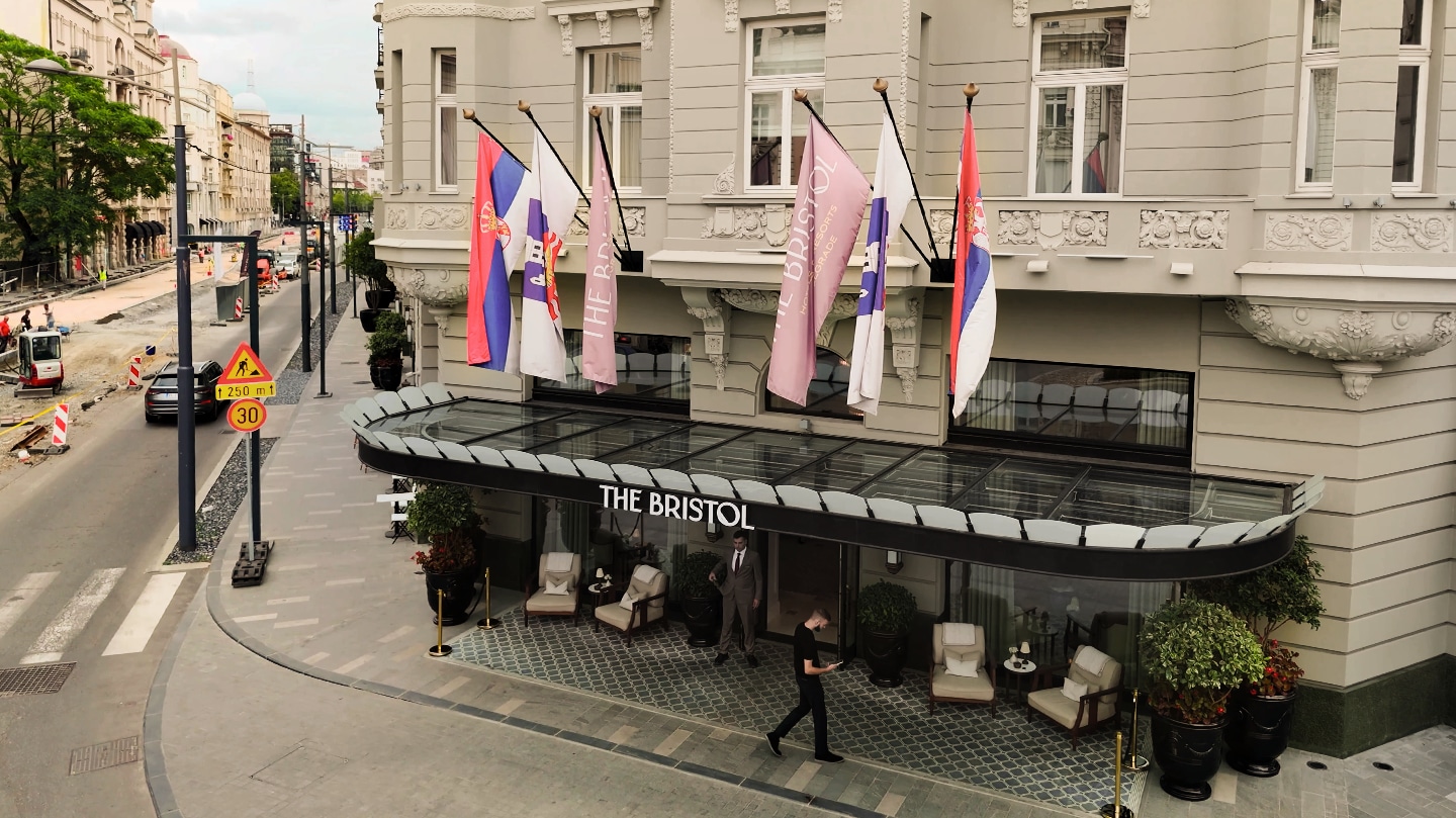 Classic facade of The Bristol Hotel in Belgrade with flags and construction zone on city street	