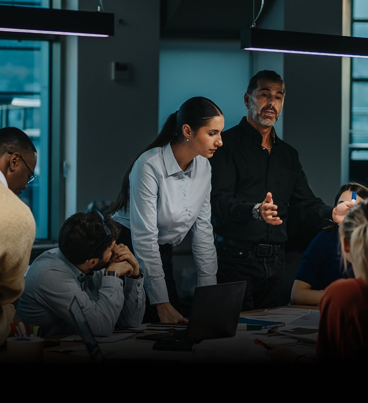 Business team in a modern office engaged in a serious discussion, with a man presenting and a woman listening attentively.