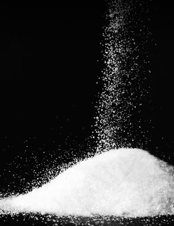 White powder particles falling against a black background, forming a pile at the bottom