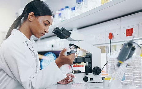 Researcher in a white lab coat working with a pipette and microscope in a laboratory.