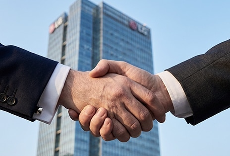 Two professionals shaking hands in front of an LG building, symbolizing long-term builder partnership.