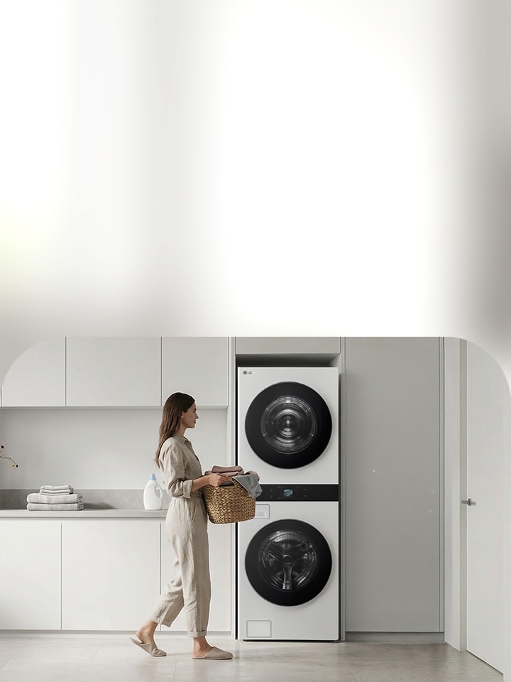 Woman carrying a laundry basket in a bright white laundry room with LG WashTower stacked washer and dryer unit