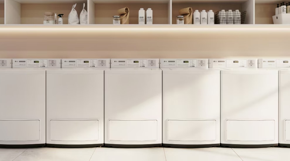 Row of white LG commercial laundry machines with shelves above holding detergent and supplies