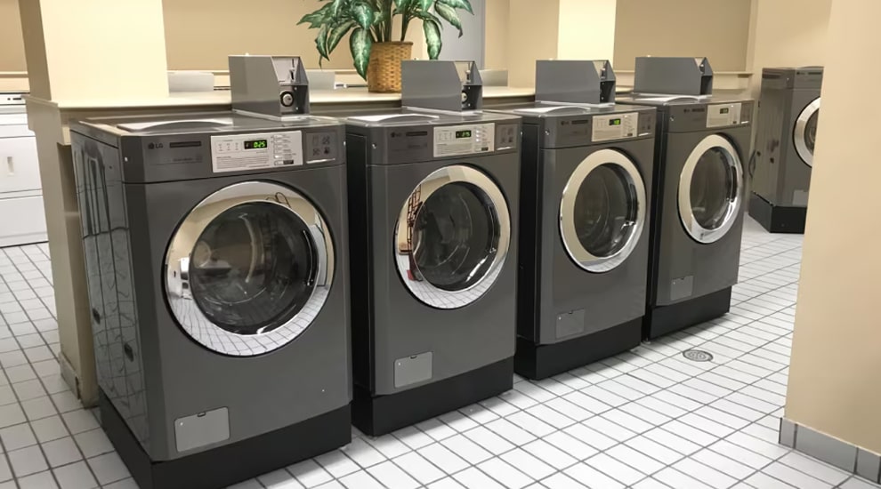 Row of LG commercial front-load washers with payment systems installed in a tiled laundry room