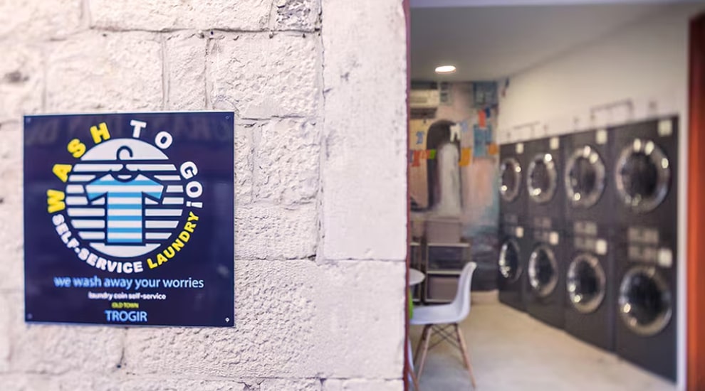 Exterior wall with Wash to Go self-service laundry sign and view into laundromat with LG washers