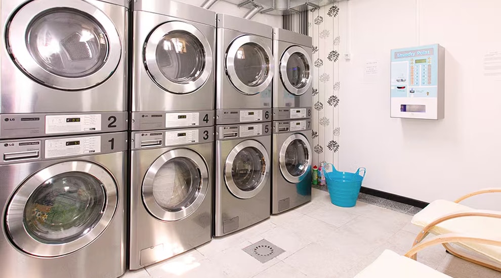 Laundromat interior with stacked LG commercial washers and dryers, detergent vending machine, and seating area