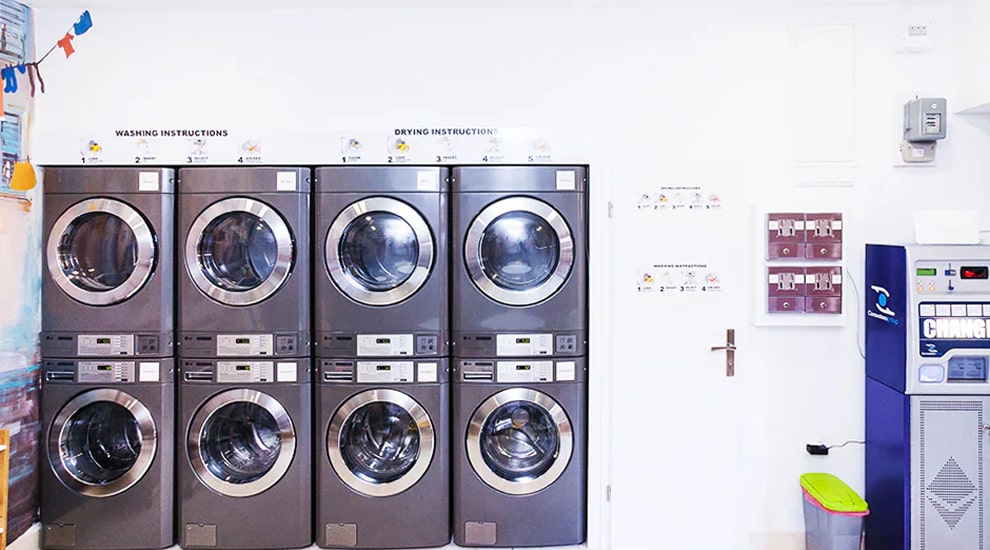 Laundromat interior with stacked LG commercial washers and dryers, washing and drying instructions on wall, and payment machine