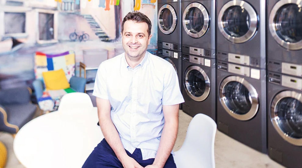 Man sitting and smiling in front of laundromat interior with rows of LG commercial washers and dryers