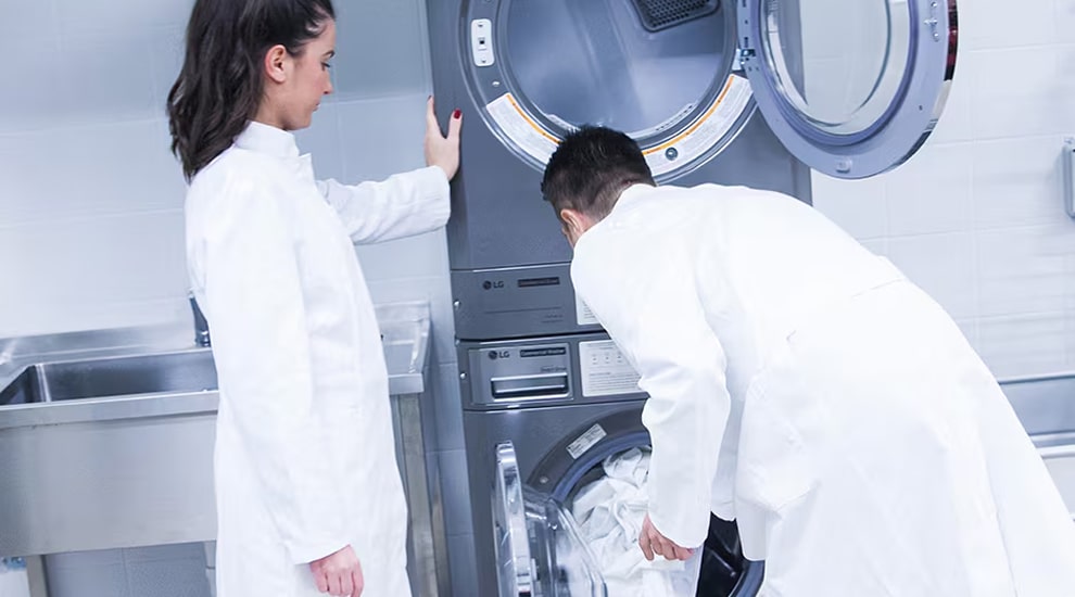 Two people in lab coats using LG stacked commercial washer and dryer in a laundry facility