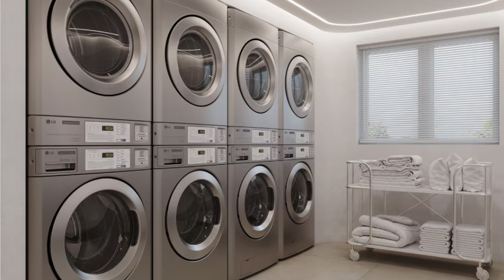 Row of LG commercial stacked washers and dryers with folded towels on cart