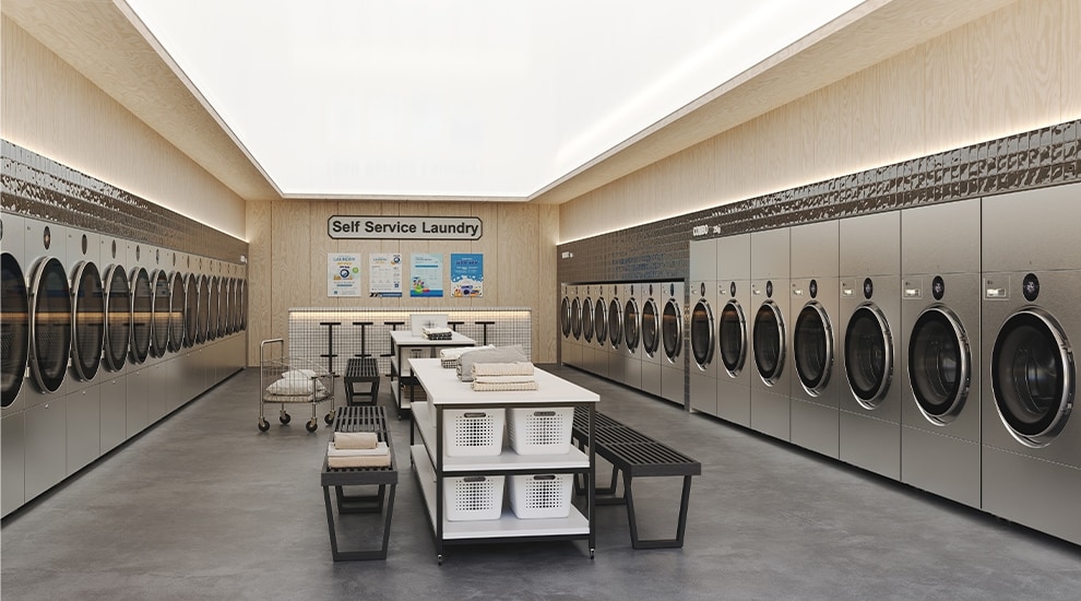 Row of white LG commercial laundry machines with shelves above holding detergent and supplies