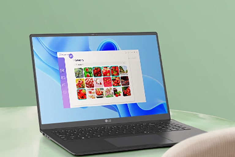 A laptop placed on a green table, displaying a gallery application interface with images of red fruits on the screen, suggesting navigation or photo management activities.