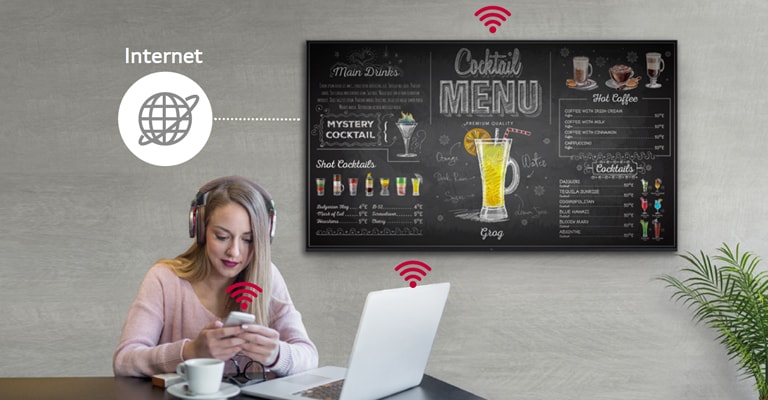 The UR3J series is on the wall and a woman is using a personal PC and mobile phone. This image shows that the signage can be connected wirelessly to the PC and mobile phone which she is holding.