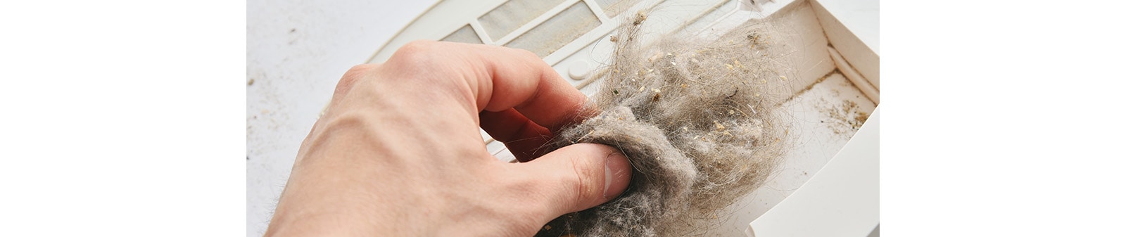 A hand taking away the dirt from vacuum cleaner's suction inlet