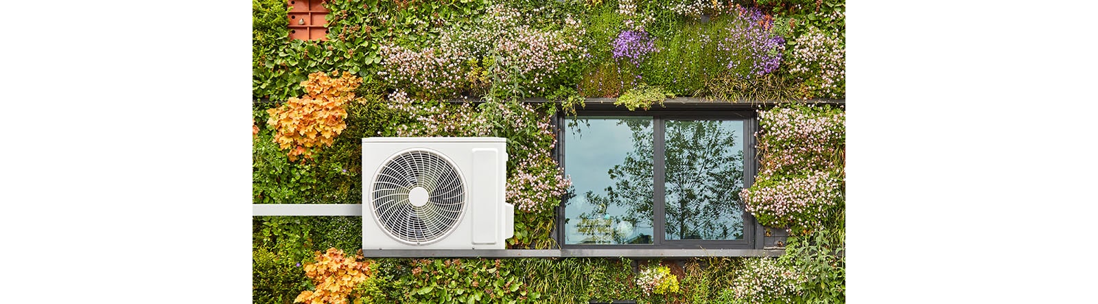 An outdoor ac unit beside the window with grass and colorful flowers as background