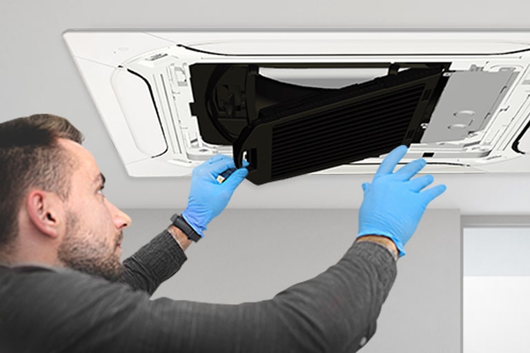 A man wearing blue nitrile gloves is replacing the black filter in an installed LG Dual Vane cassette.