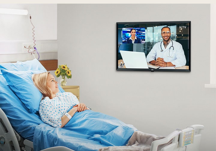 The patient is lying in the hospital room’s bed and watchiccng the TV hanging on the wall.