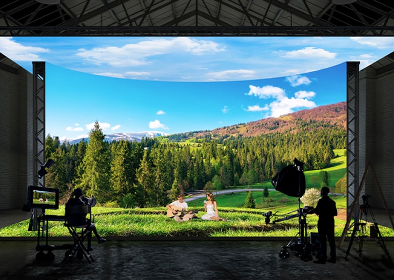 A virtual production studio with curved LED walls and ceiling and floor LEDs is filming images of a forest and field landscape.