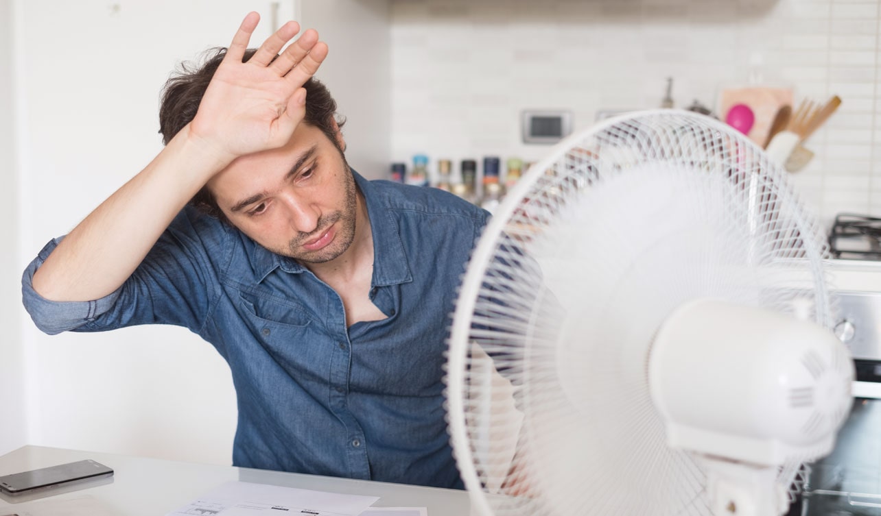 A man enjoys the breeze from an electric fan
