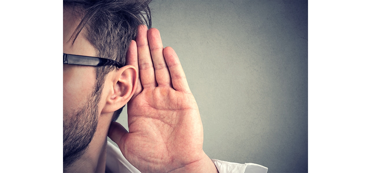 A person putting his had by his ear to listen carefully
