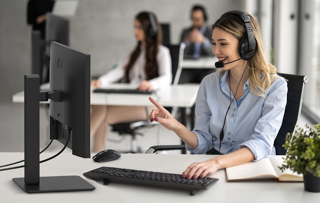 A woman is wearing a headset and working while looking at a monitor.	