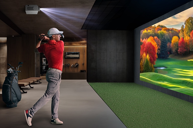 There is an indoor golf simulator with a golfer swinging and a vibrant autumn landscape projected on the wall.