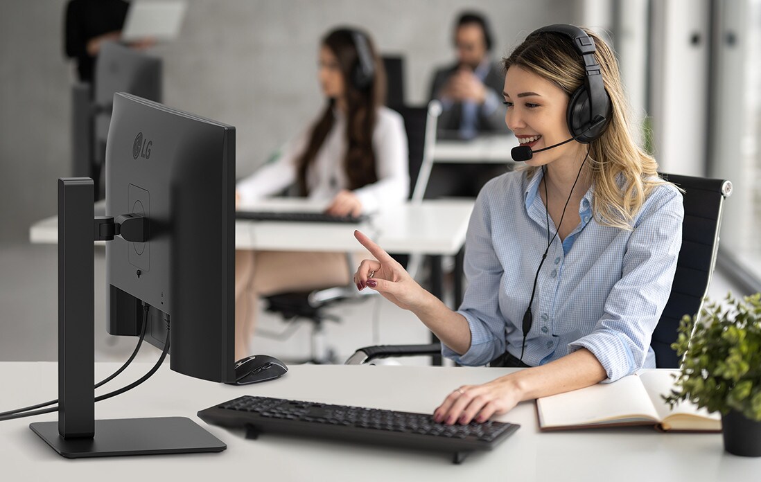 A woman is wearing a headset and working while looking at a monitor.