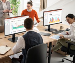 Employees sitting at office desks and having a conversation.	