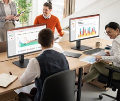 Employees sitting at office desks and having a conversation.	