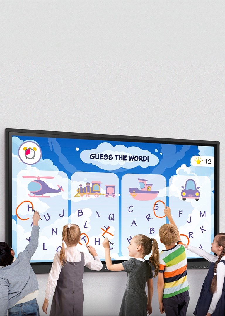 Group of children standing in front of a large interactive LG digital board, playing an educational word guessing game by touching letters on the screen