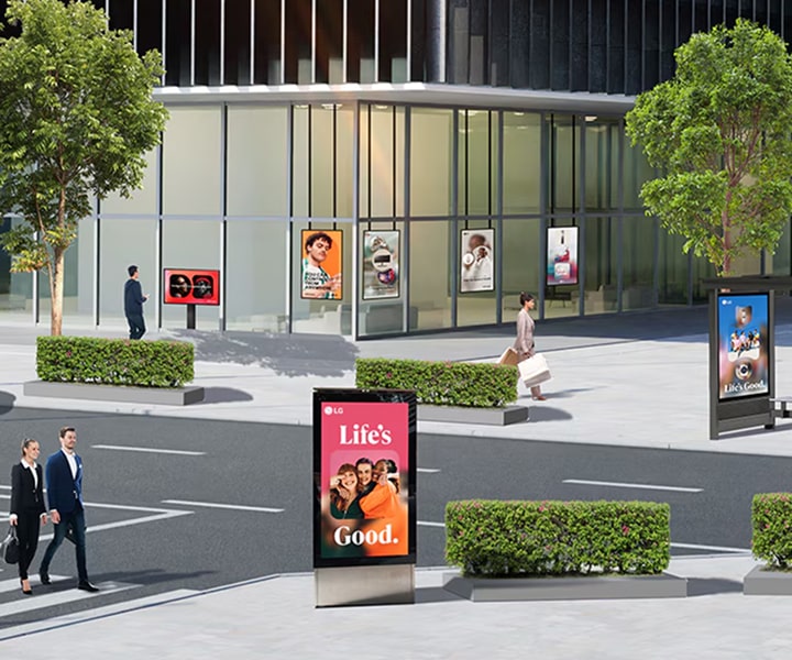 Modern glass building in an urban area with multiple LG digital billboards and posters displaying advertisements, including 'Life’s Good,' positioned along the sidewalk and near the entrance