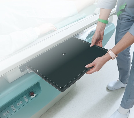 Nurse inserting a portable LG digital X-ray detector panel into hospital imaging equipment for patient examination.